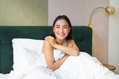 Portrait of young woman sitting on bed at home