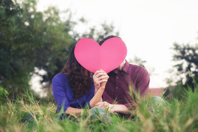 Couple holding heart shape while sitting at park