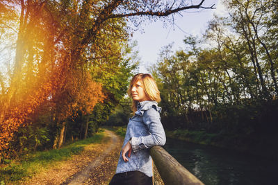 Woman looking away against trees during sunset