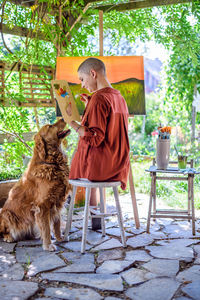 Artist working on painting outdoors in her garden with golden retriever keeping her company. 