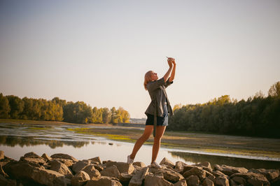 Woman photographing with mobile phone by lake