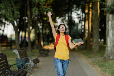 A happy young girl with a book in her hands walks through the park after lectures at the university