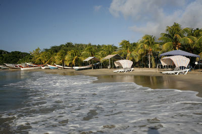 Lounge chairs by moored boats at beach against sky