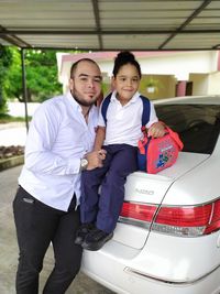 Portrait of father and daughter standing by car