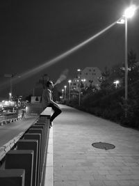 Man smoking while sitting on railing by footpath at night