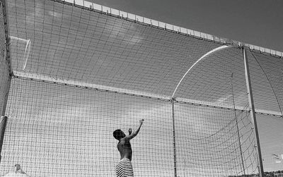 Low angle view of shirtless man standing amidst net against sky