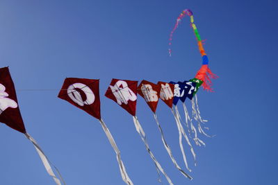 Low angle view of flags hanging against clear blue sky