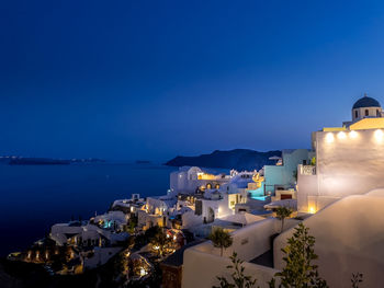 Illuminated buildings by sea against clear blue sky at night