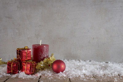 Christmas presents and candle with fake snow against wall on table