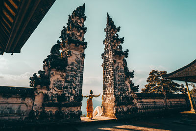 Rear view of woman standing amidst built structure at temple against sky