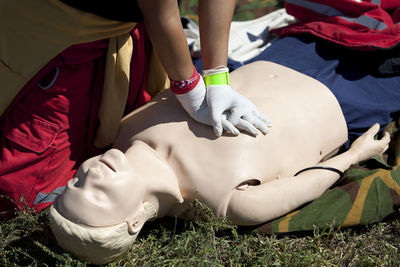 Low section of man practicing cpr on dummy at field during sunny day