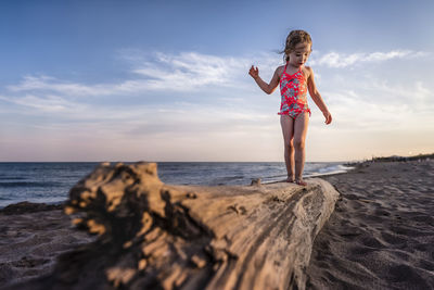 Girl balancing on drift wood log at the beach looks down