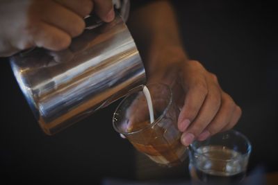 Midsection of person pouring milk in coffee