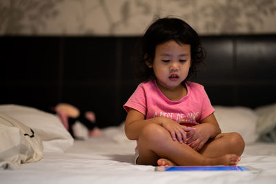 Girl using digital tablet while sitting on bed 