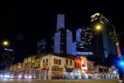 Illuminated buildings by street against sky at night