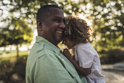 Happy father embracing son while standing against trees at park