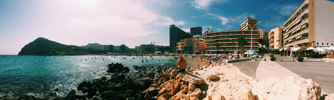 building exterior, architecture, built structure, water, sky, city, panoramic, large group of people, sea, incidental people, city life, cloud - sky, sunlight, travel, travel destinations, cloud, tourism, outdoors, person