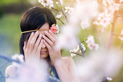 Close-up of woman covering eyes with her hands by cherry tree