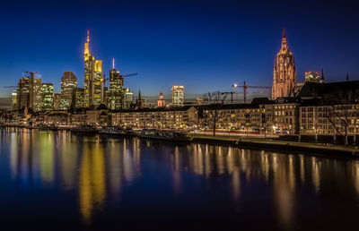 River by illuminated modern city against sky at dusk