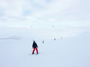 People skiing on snow covered landscape against sky