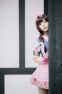 Woman looking away while standing against pink wall