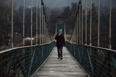 Full length of man walking on footbridge in forest