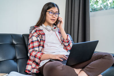 Full length of senior woman using phone while sitting on sofa