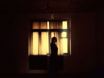 Side view of silhouette woman standing against window at home