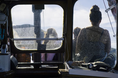 Rear view of woman sitting on boat seen through window