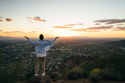 Rear view of man standing on landscape against sky during sunset