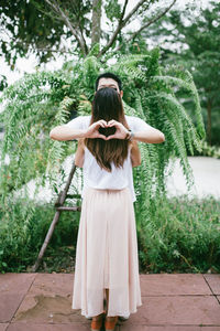 Rear view of woman with arms outstretched standing against plants