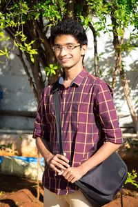 Portrait of smiling young man with shoulder bag standing outdoors