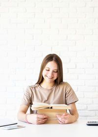 Portrait of a smiling young woman holding smart phone against wall