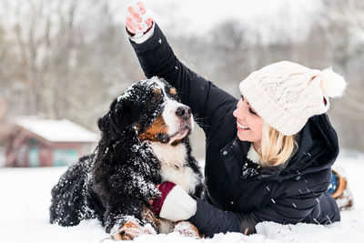 Woman playing with dog on snow covered land during winter