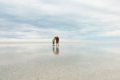 Couple standing at beach against cloudy sky