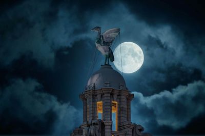 Low angle view of statue by building against sky at night