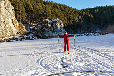 Young man skiing along  frozen snowy river near beautiful cliffs with pine forest. winter activities 