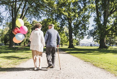 Back view of senior couple with balloons strolling in a park