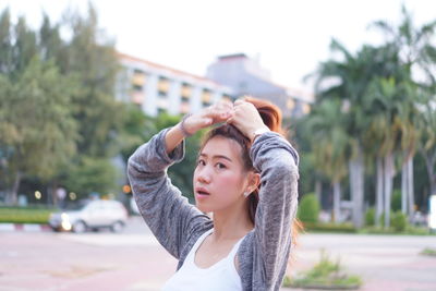 Portrait of young woman tying hair at city
