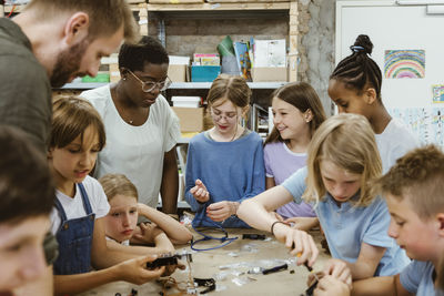 Group of students and teacher assisting each other while working on robotics project at workshop in school