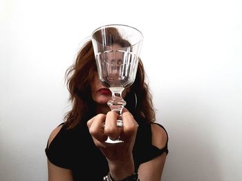 Portrait of young woman drinking glass against white background