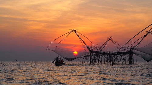 Silhouette fishing net on sea against sky during sunset