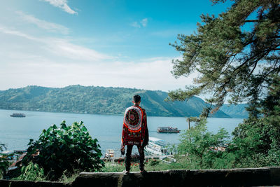 Rear view of man standing by tree against sky