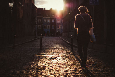 Rear view of woman walking on street amidst buildings during sunset