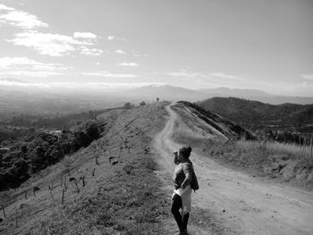 Woman standing by dirt road on mountain against sky