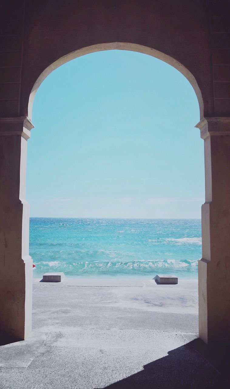 sea, arch, horizon over water, water, nautical vessel, clear sky, built structure, indoors, architecture, transportation, blue, window, scenics, archway, tranquil scene, vacations, motorboat, tourism, tranquility, day, seascape, sky, nature, entrance, arched, shore, seashore