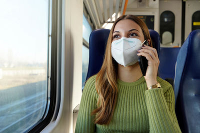 Woman wearing protective mask required for public transport talking with phone sitting in the train