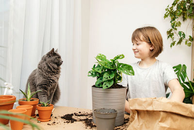 A teenage girl with a cat gardener transplants a monstera flower at home into another pot