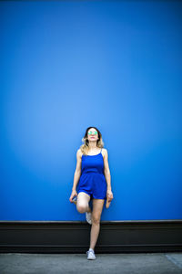 Full length of fashionable woman standing against blue wall