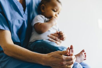 Midsection of female doctor holding baby boy while sitting against white background